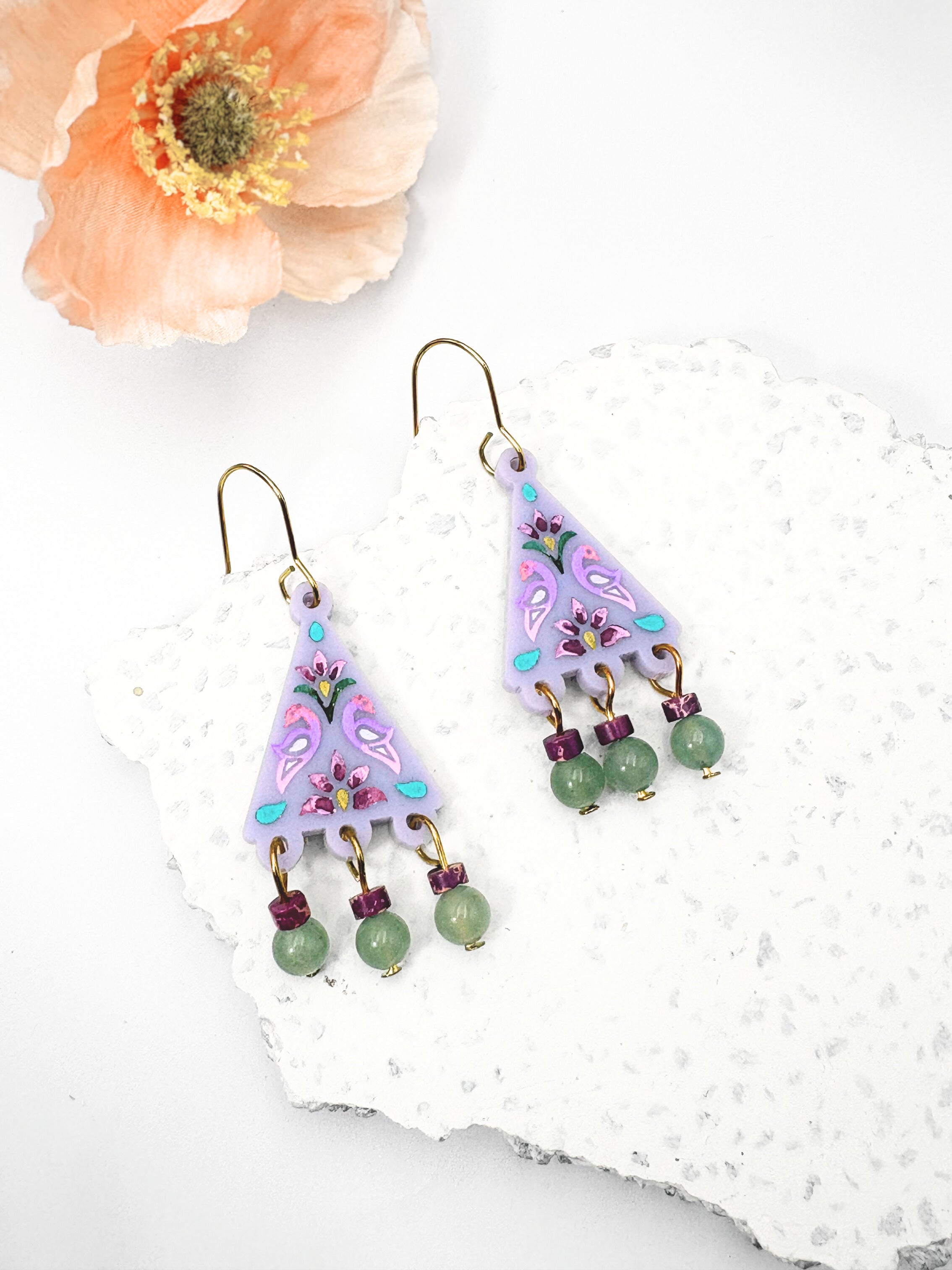 Pair of colorful earrings with floral patterns on a white surface with a flower in the background.