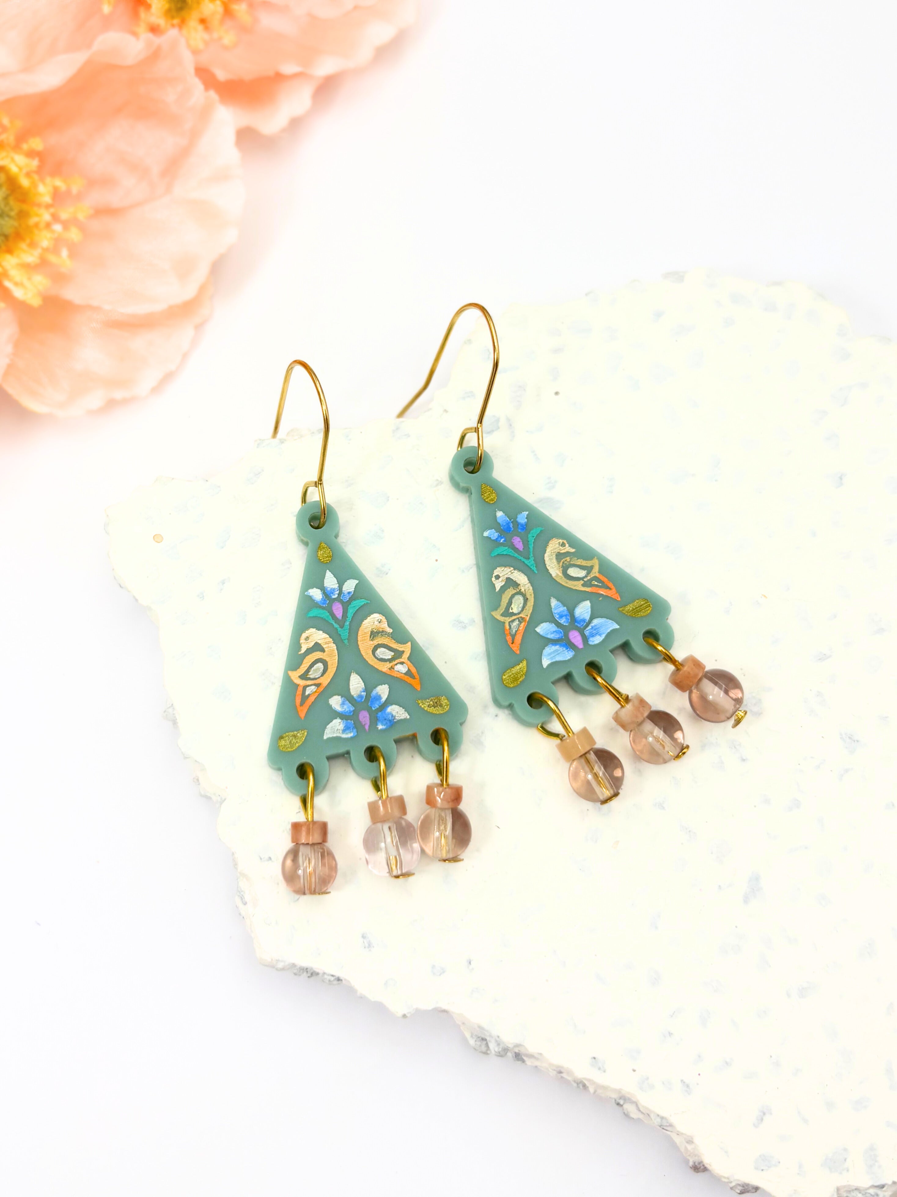 Decorative earrings with green triangular design and bead accents on a white background.