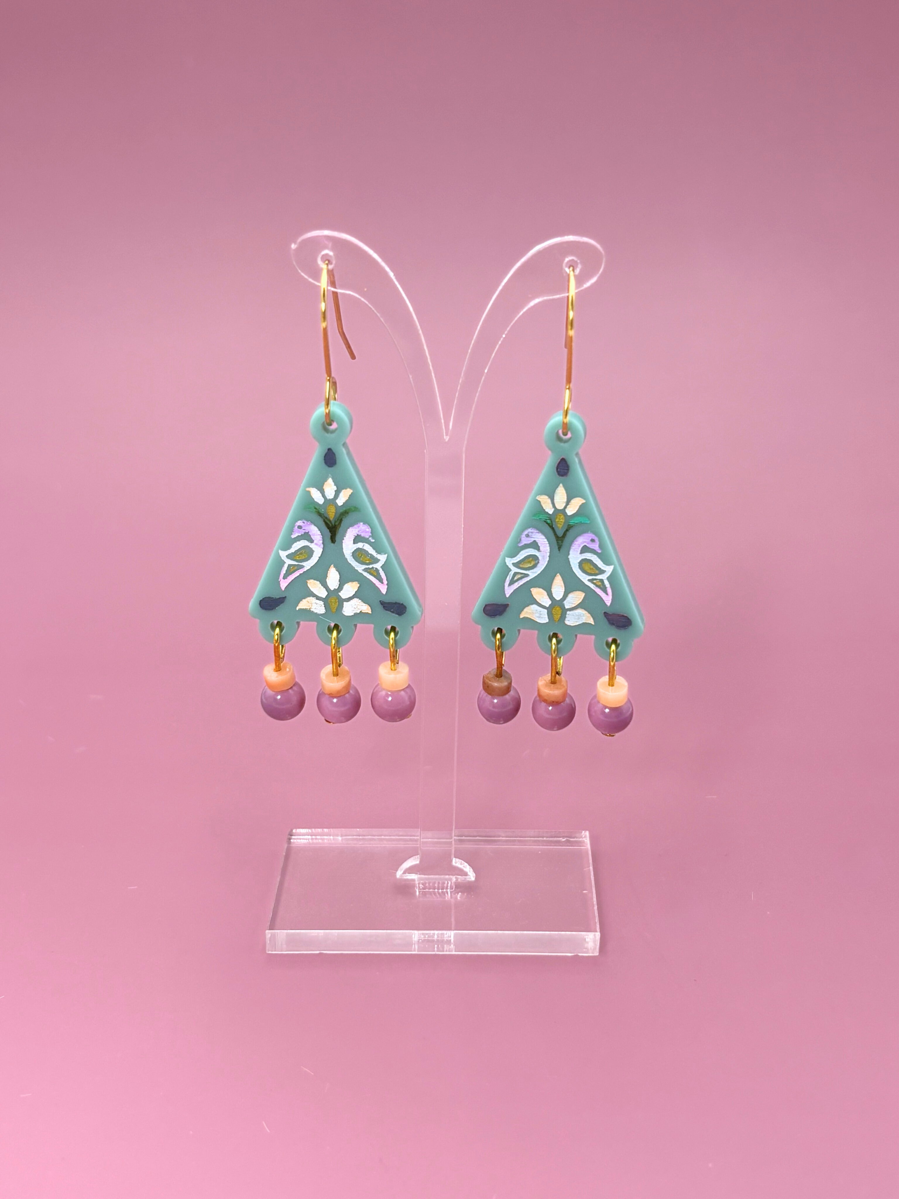 Pair of turquoise earrings with purple beads on a pink background