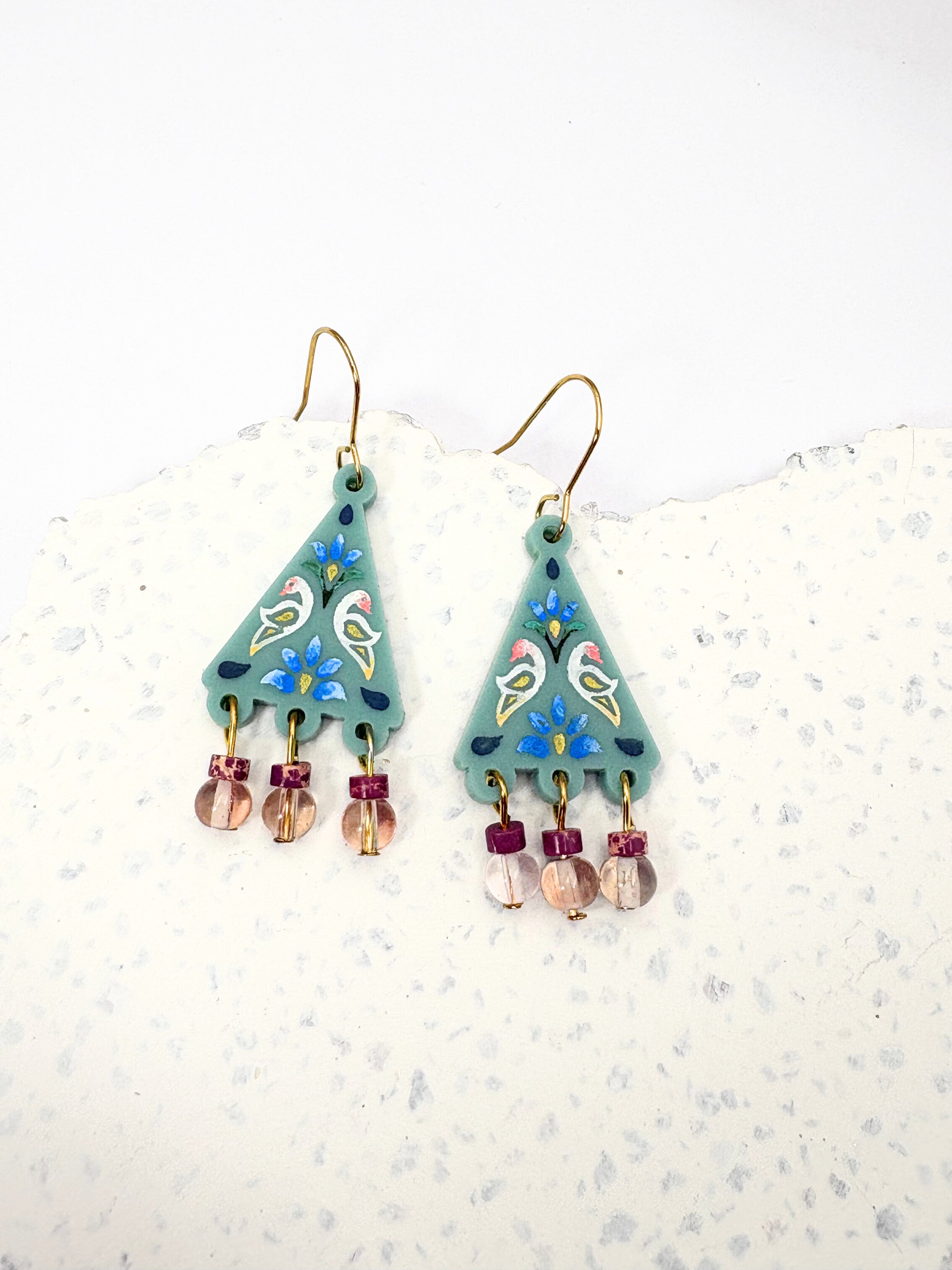 Pair of earrings with green teardrop shapes and colorful beads on a white background