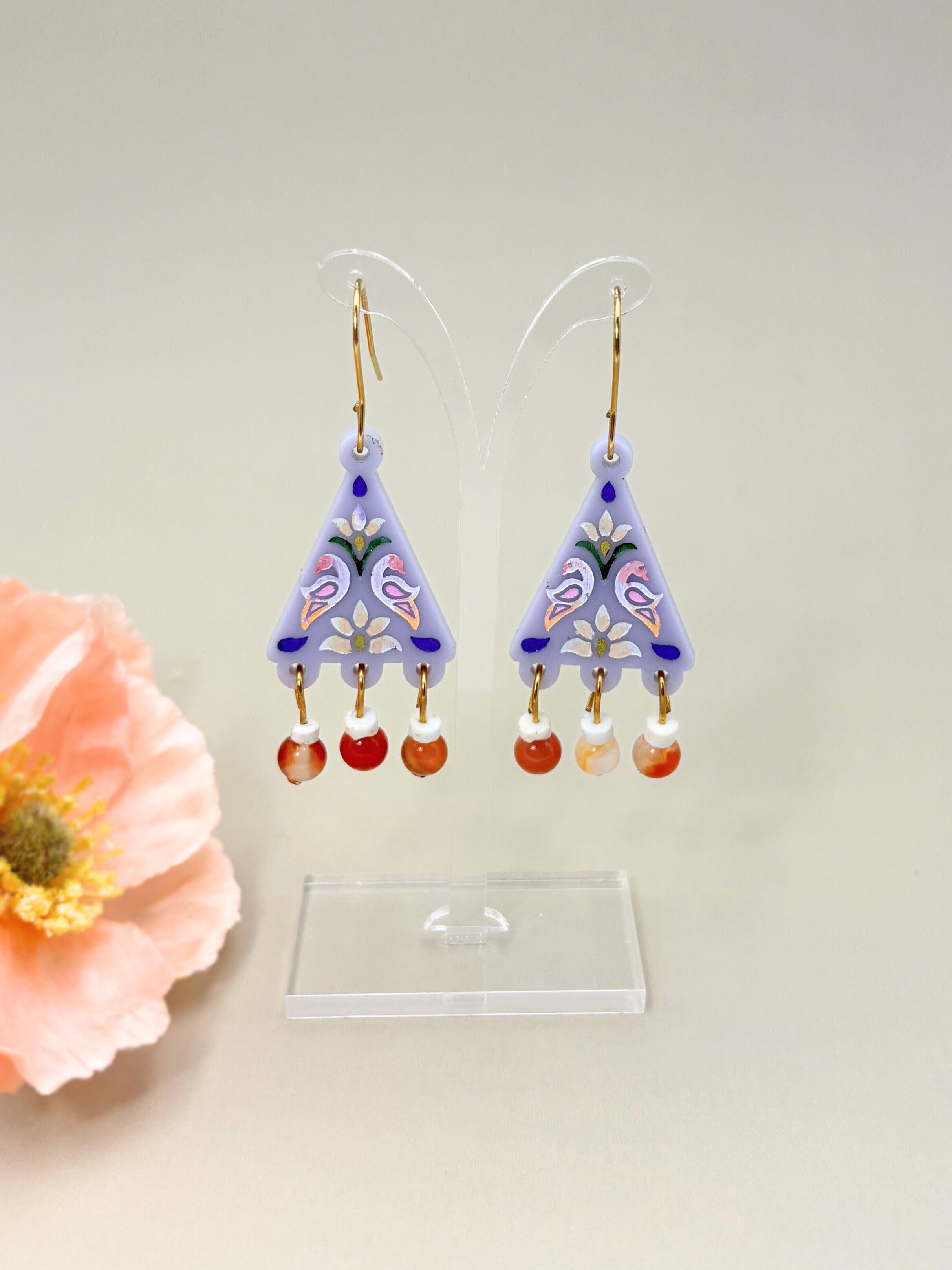 Decorative earrings on a stand with a pink flower beside them