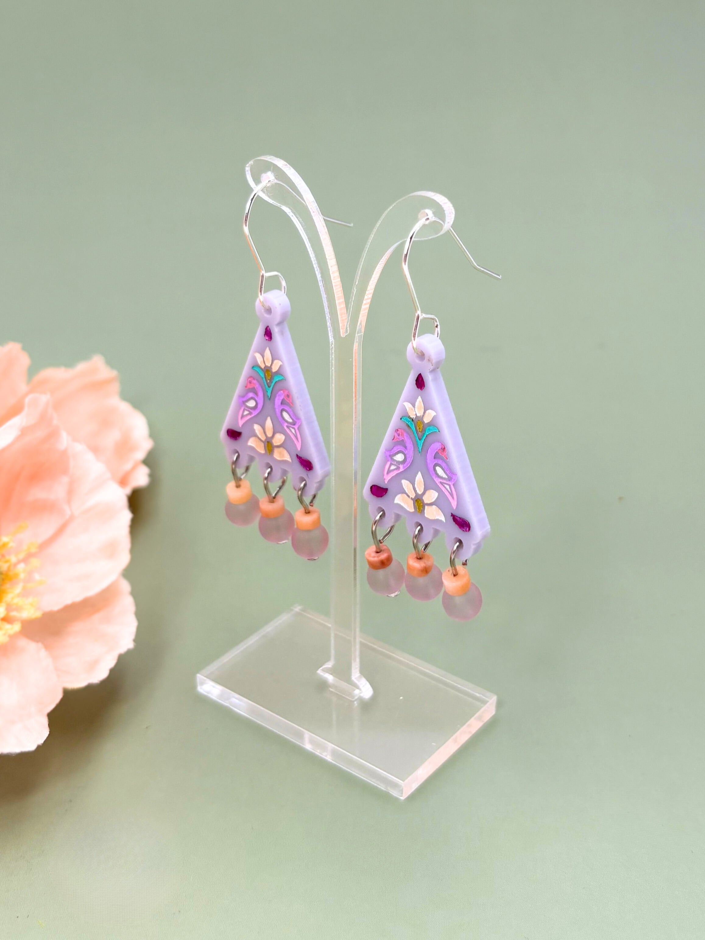 Pair of purple floral earrings on a stand with a light green background