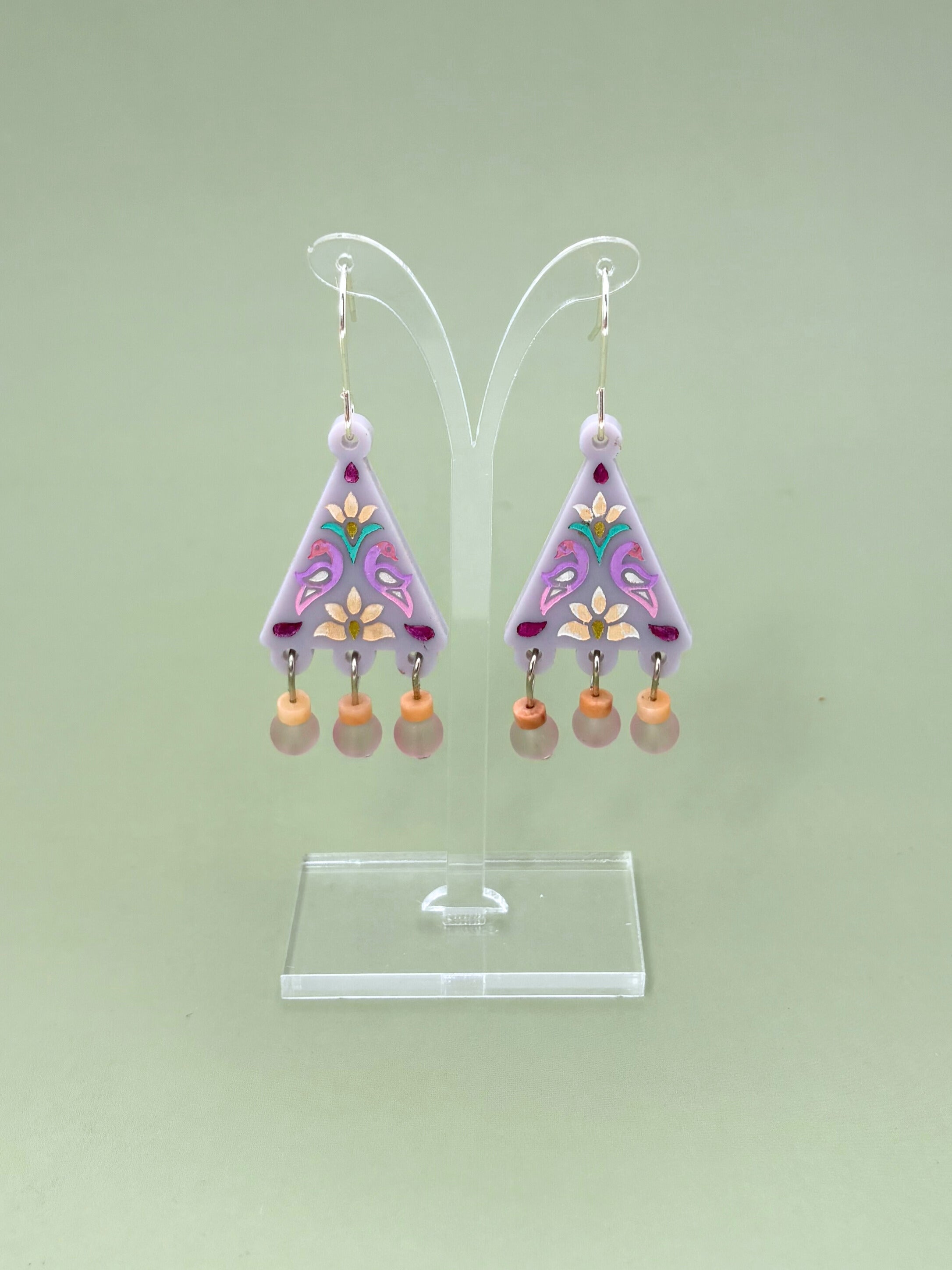 Pair of earrings on a clear stand against a light green background