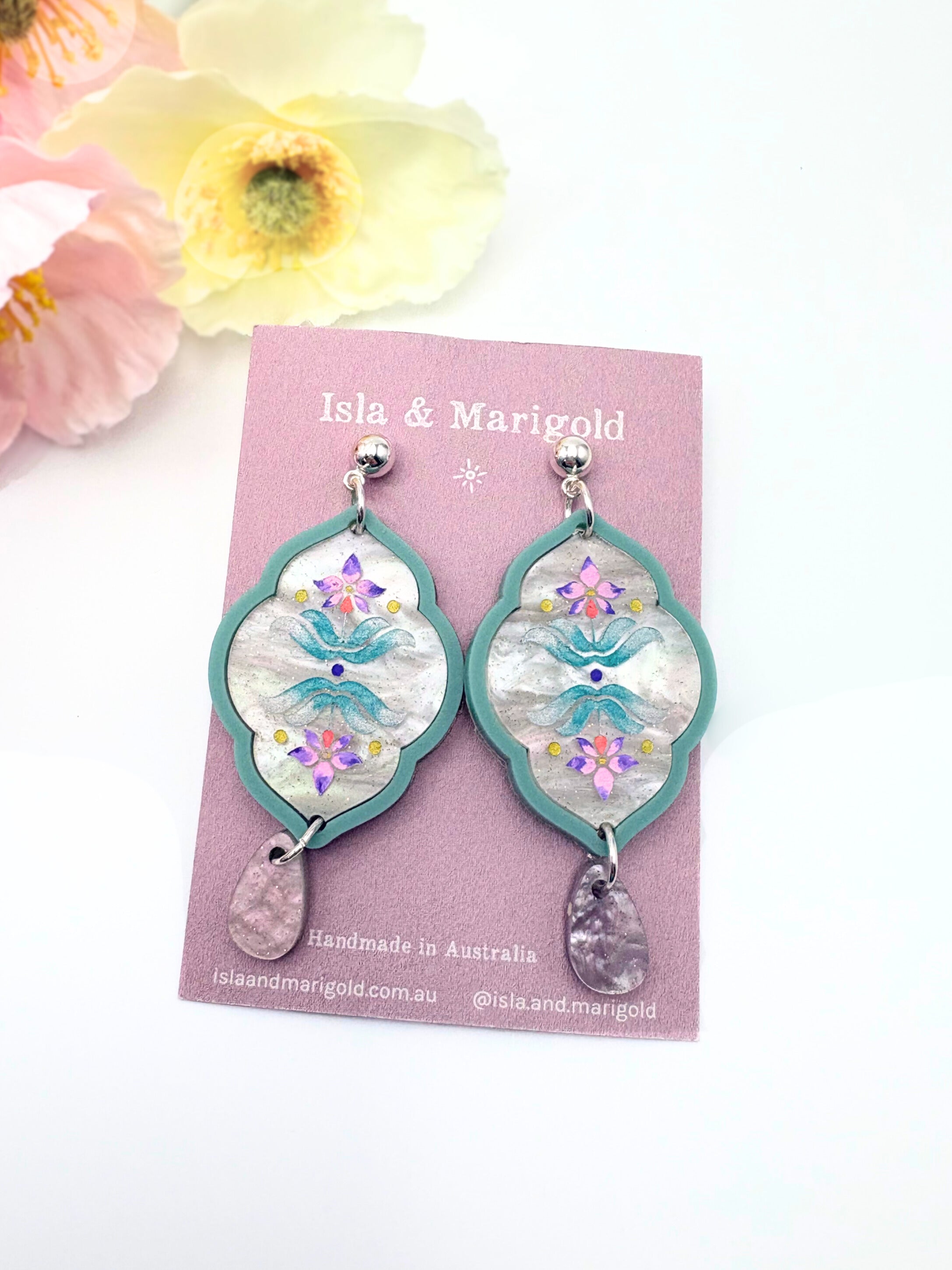 Pair of earrings on a 'Isla & Marigold' branded card with flowers in the background