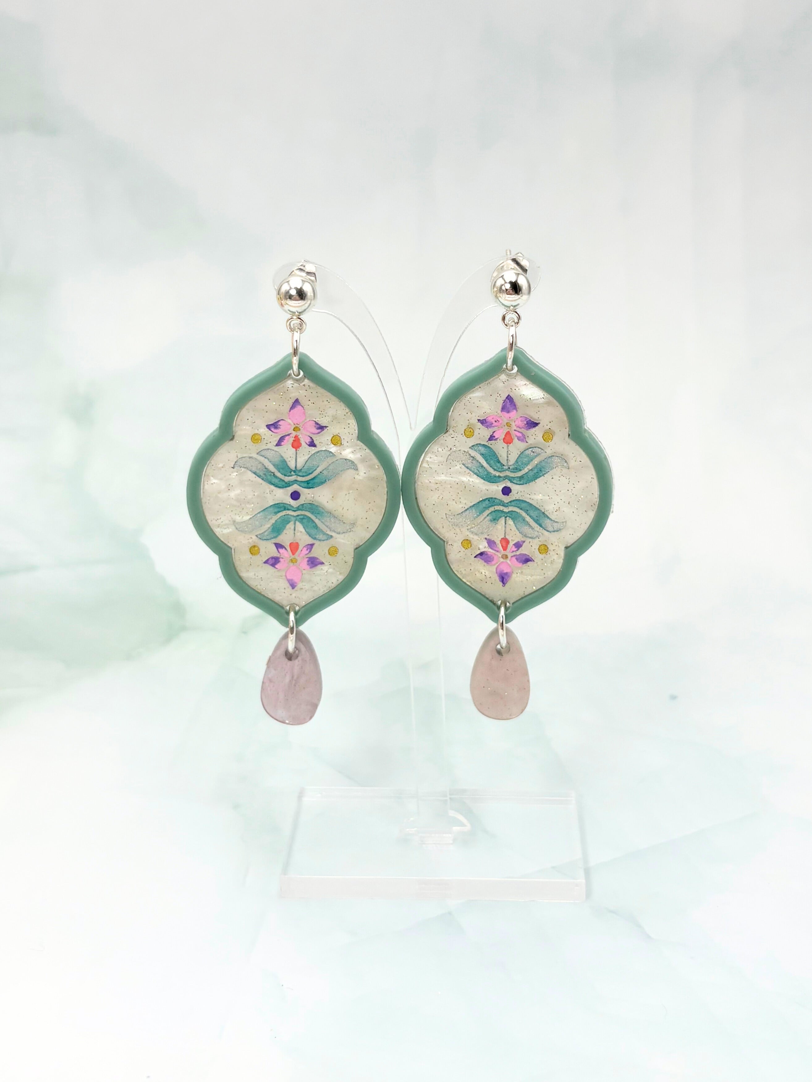 Decorative earrings with floral design and pink stones on a light background