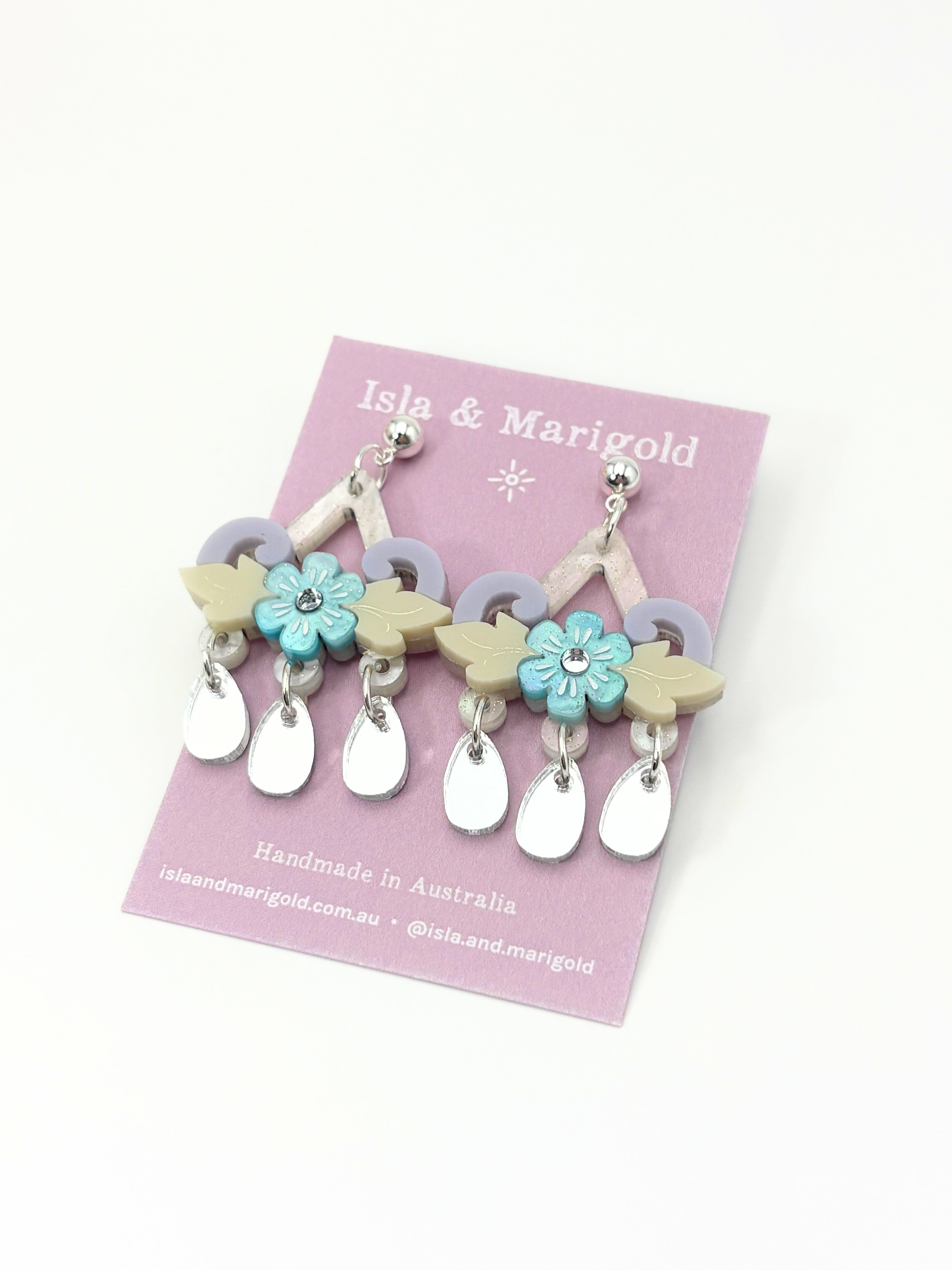 Acrylic and stainless steel earrings with floral and leaf designs on a pink card with 'Isla & Marigold' branding.