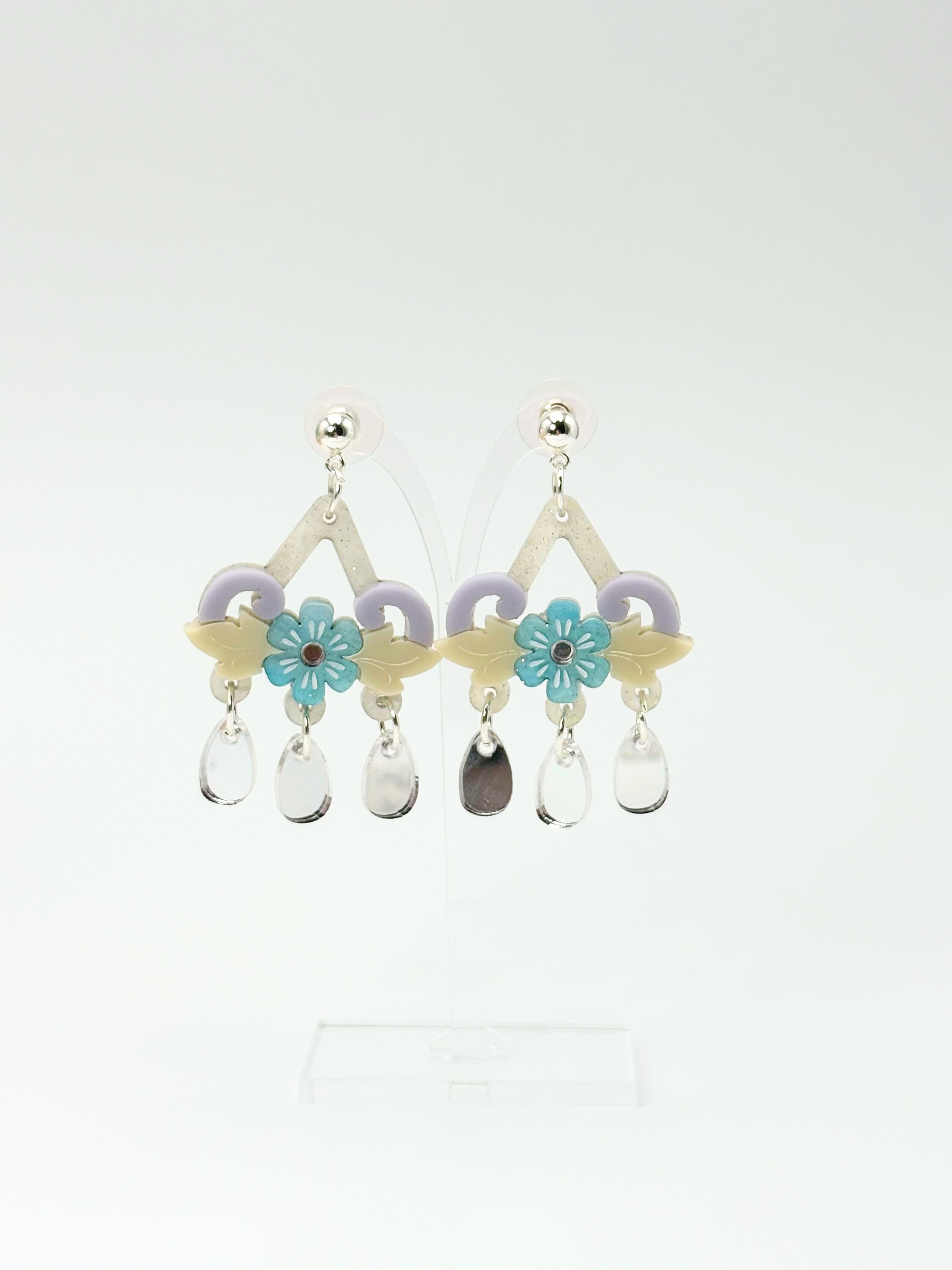 Decorative acrylic and silver earrings with floral and teardrop designs on a white background