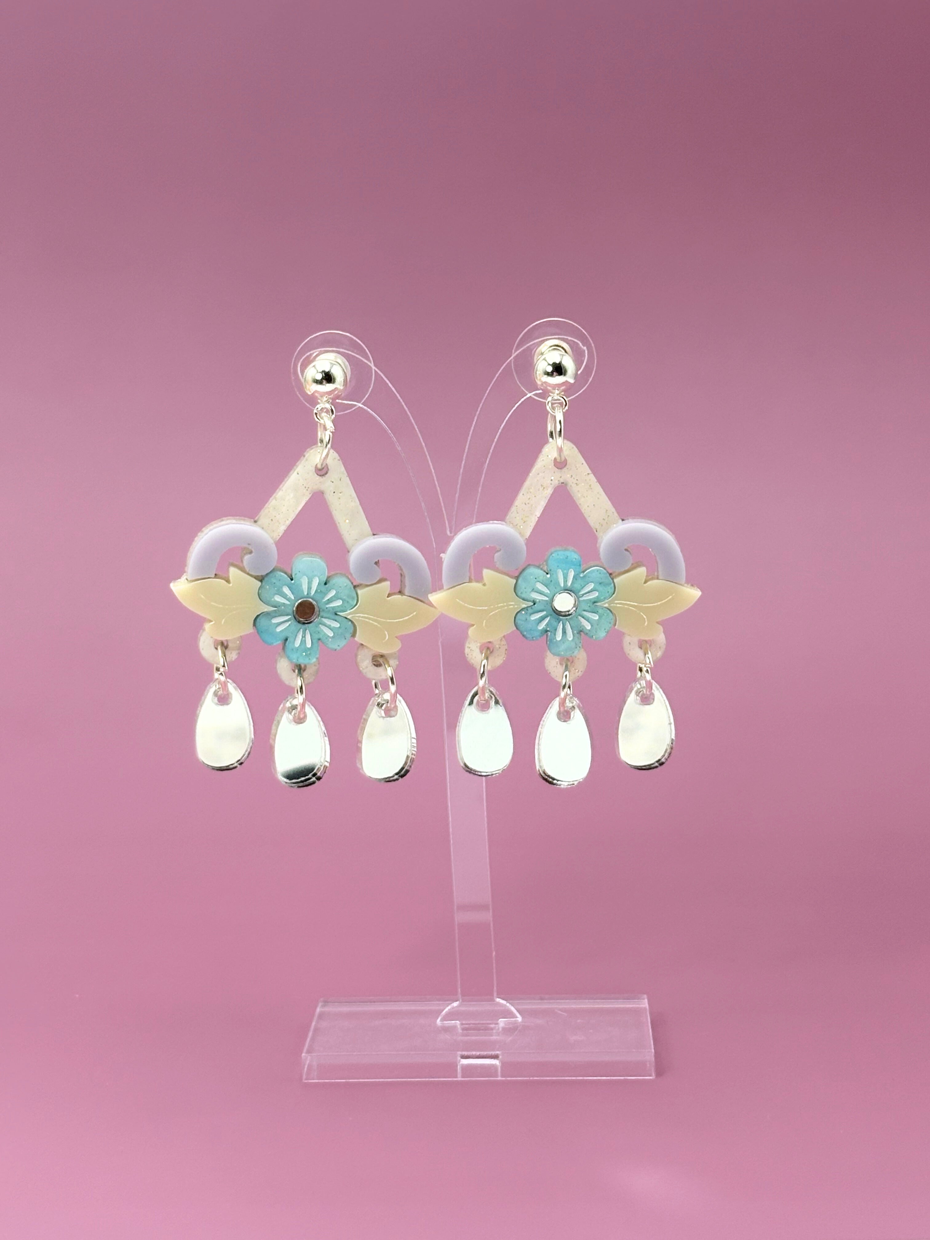 Pair of earrings on a clear stand against a pink background