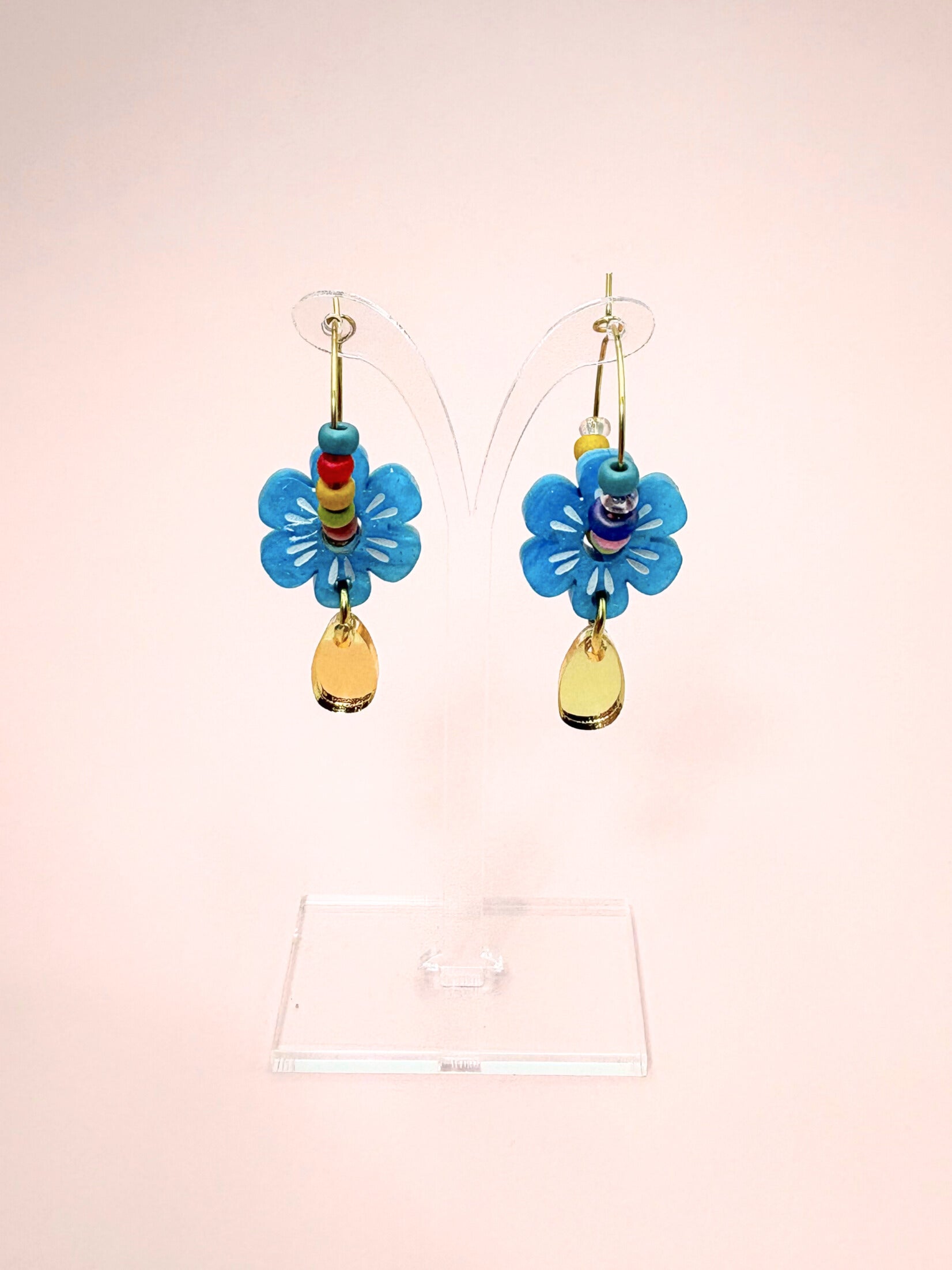 Colorful butterfly-shaped earrings on a clear stand against a light pink background