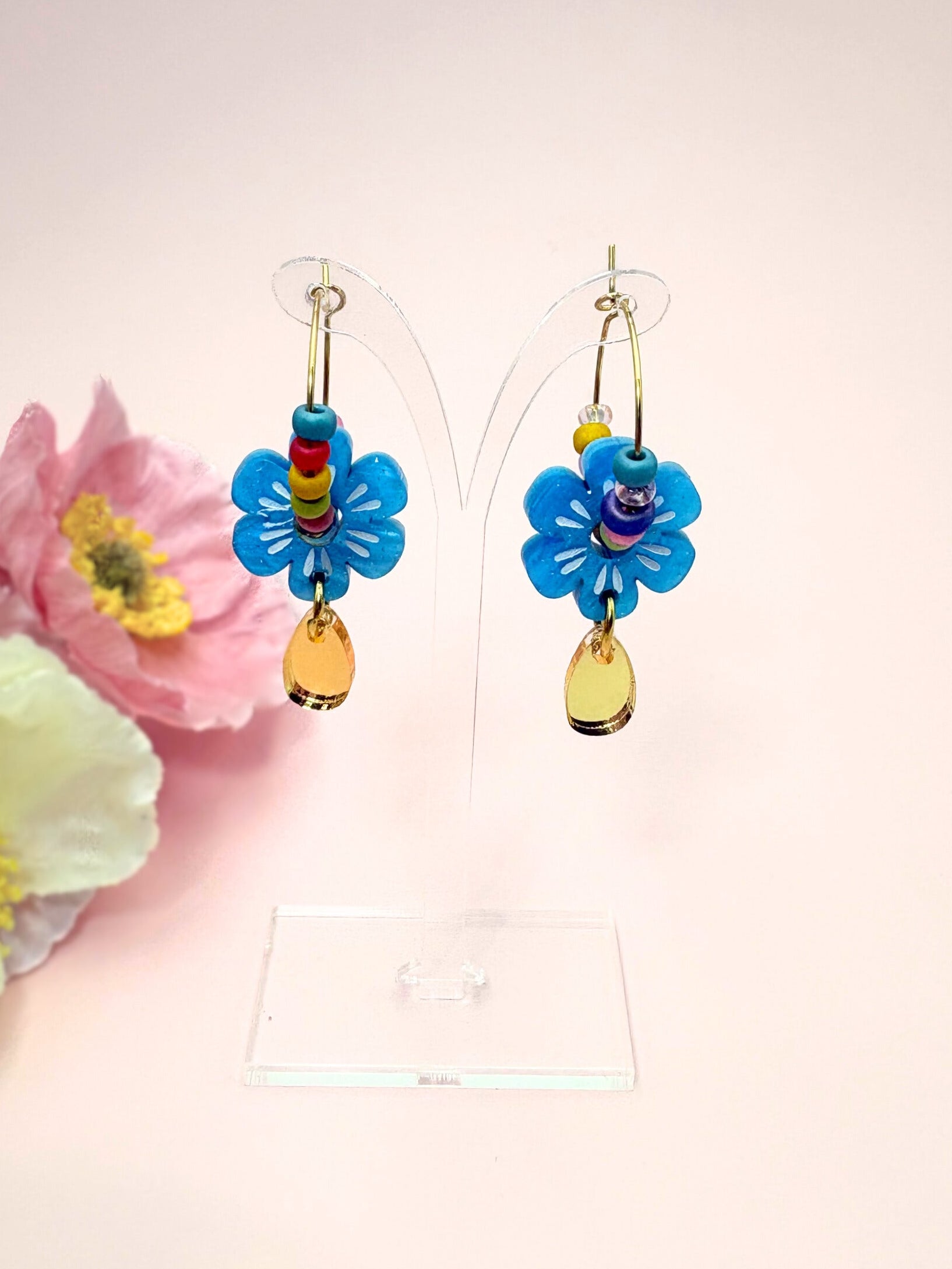 Colorful flower-shaped earrings on a stand with pink flowers in the background