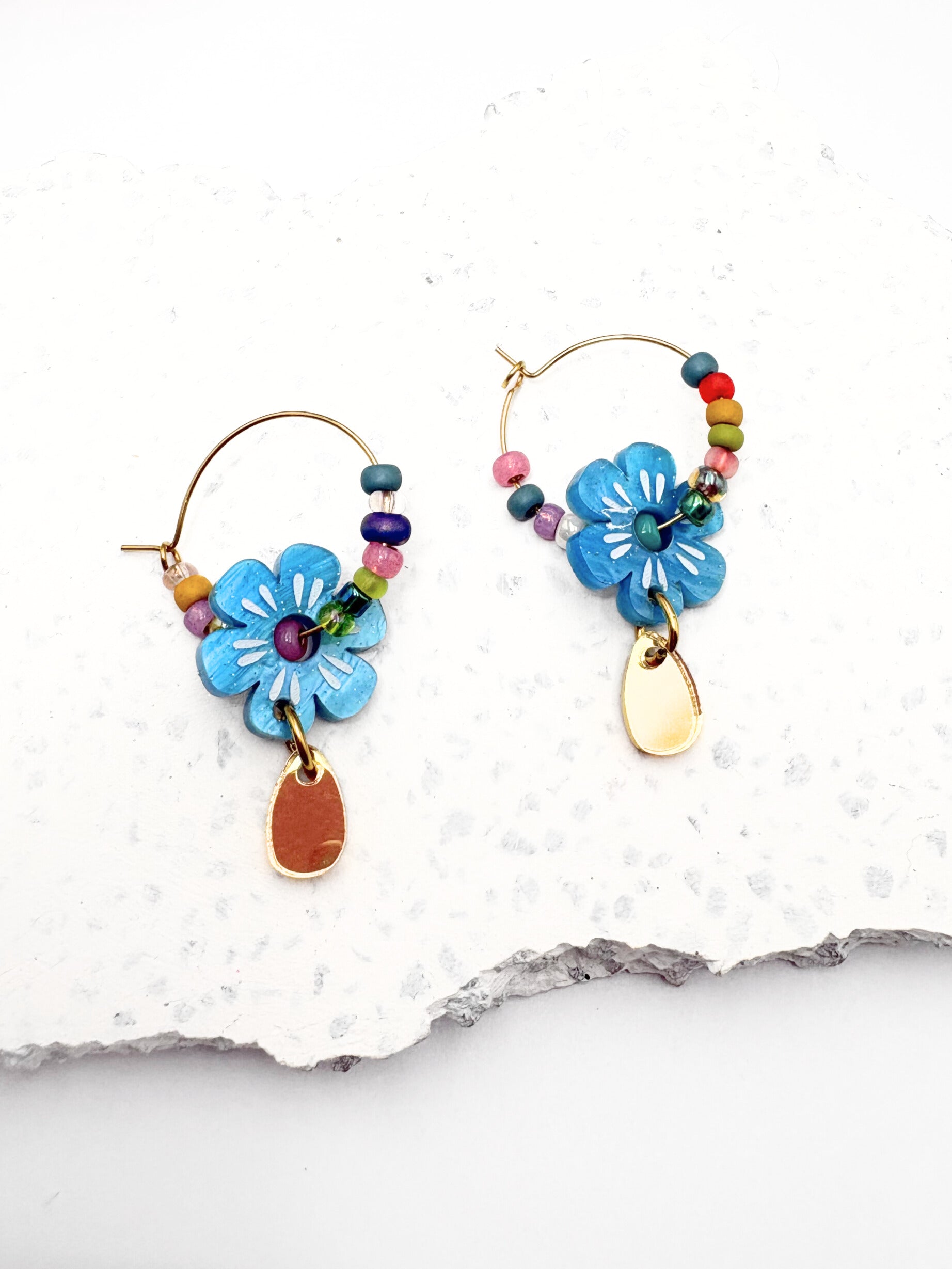 Colorful flower-shaped earrings on a white stone surface