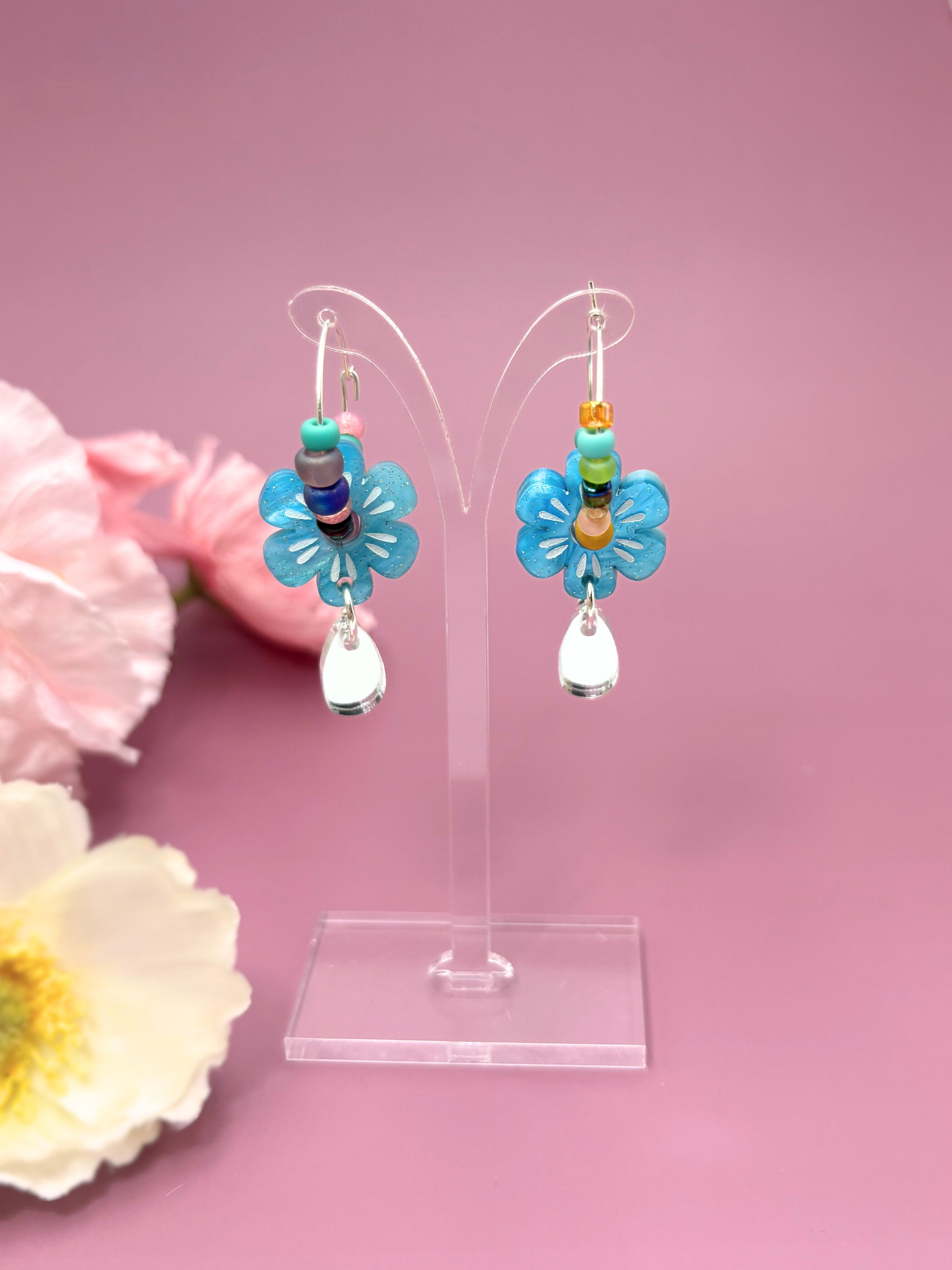 Colorful flower-shaped earrings on a clear stand with pink background