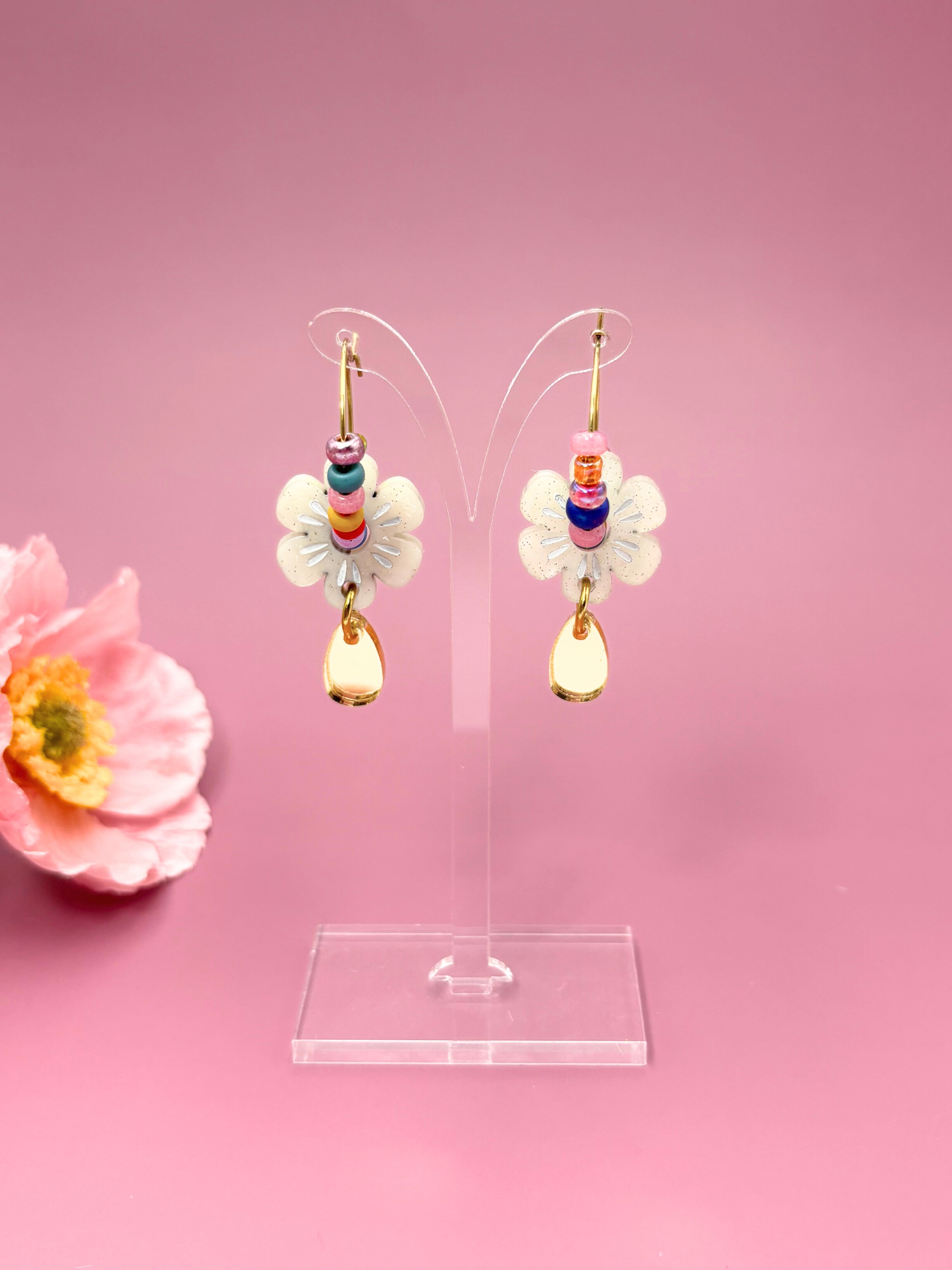 Colorful flower-shaped earrings on a clear stand with a pink background
