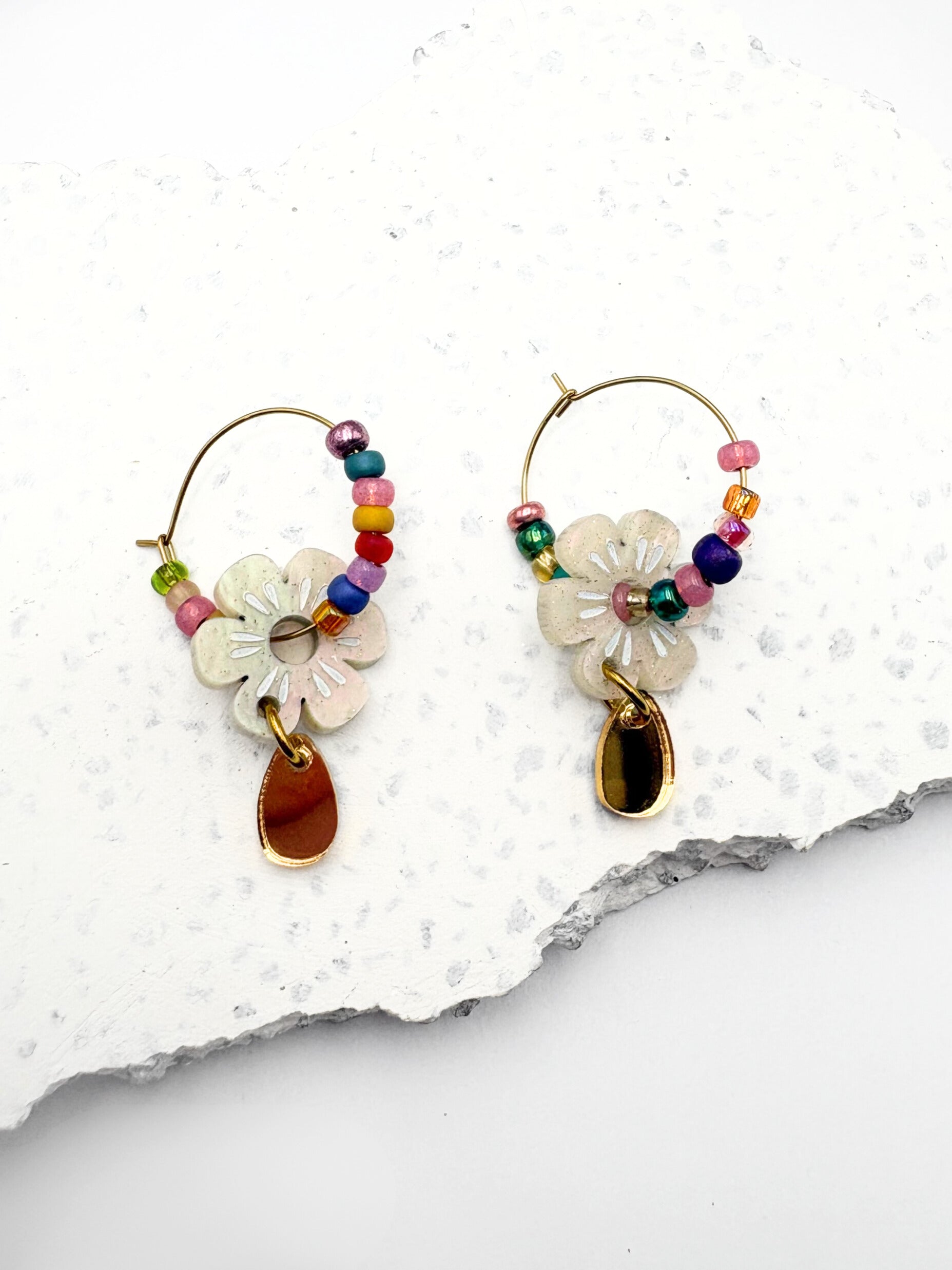 Colorful hoop earrings with floral and teardrop charms on a textured white surface