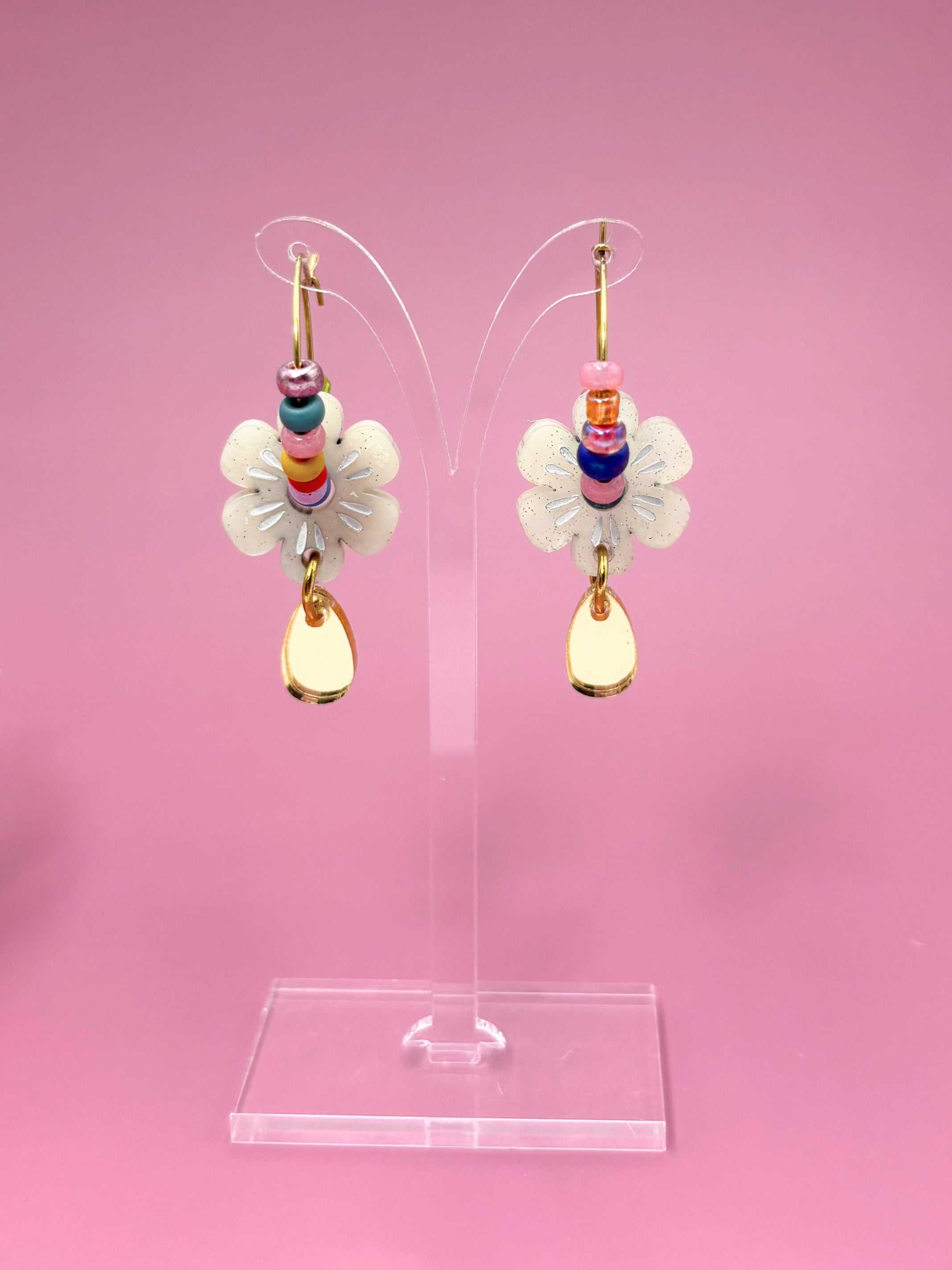 Pair of earrings with colorful beads and white flowers on a pink background
