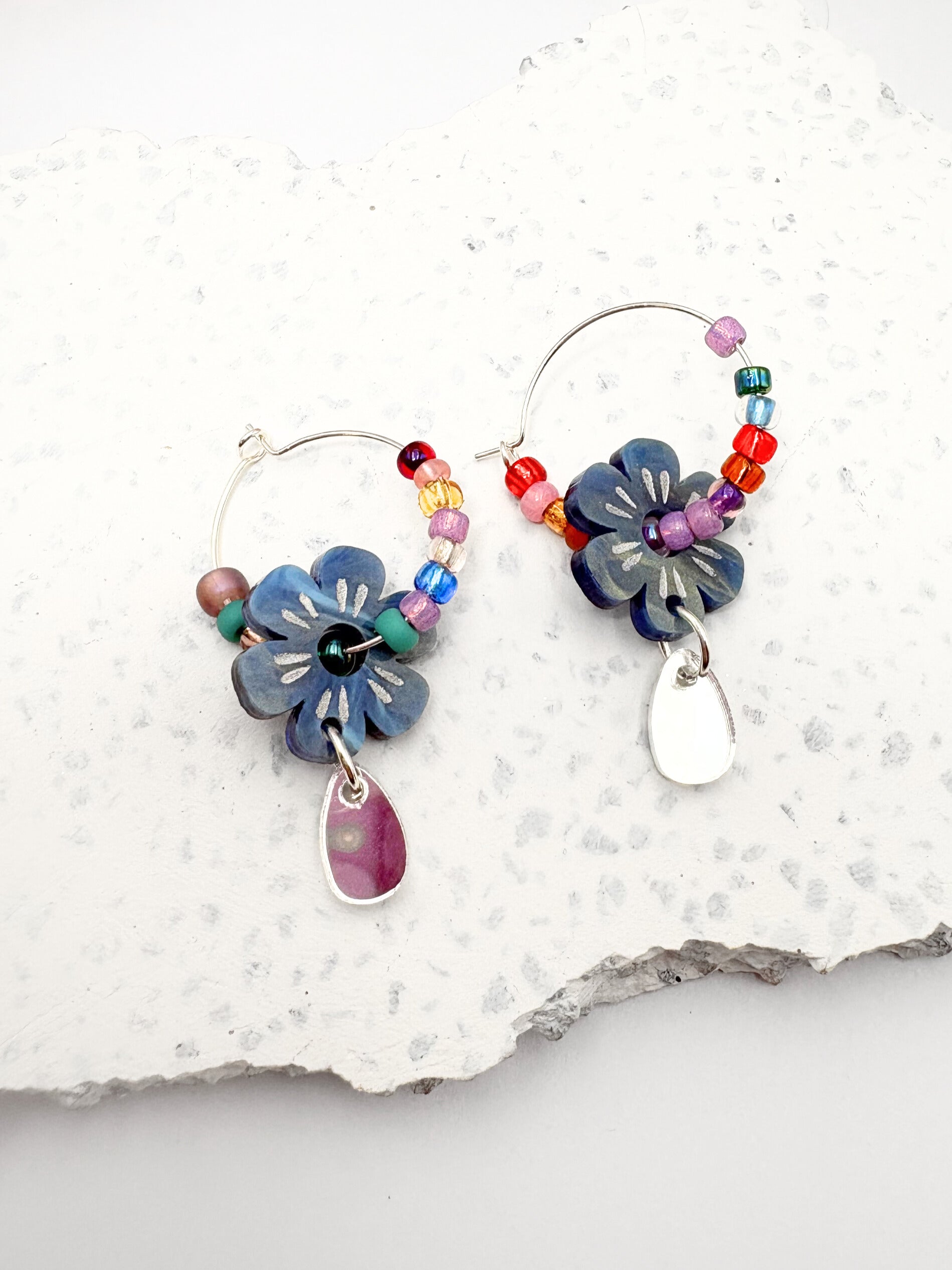 Colorful flower-shaped earrings with beads on a textured white surface