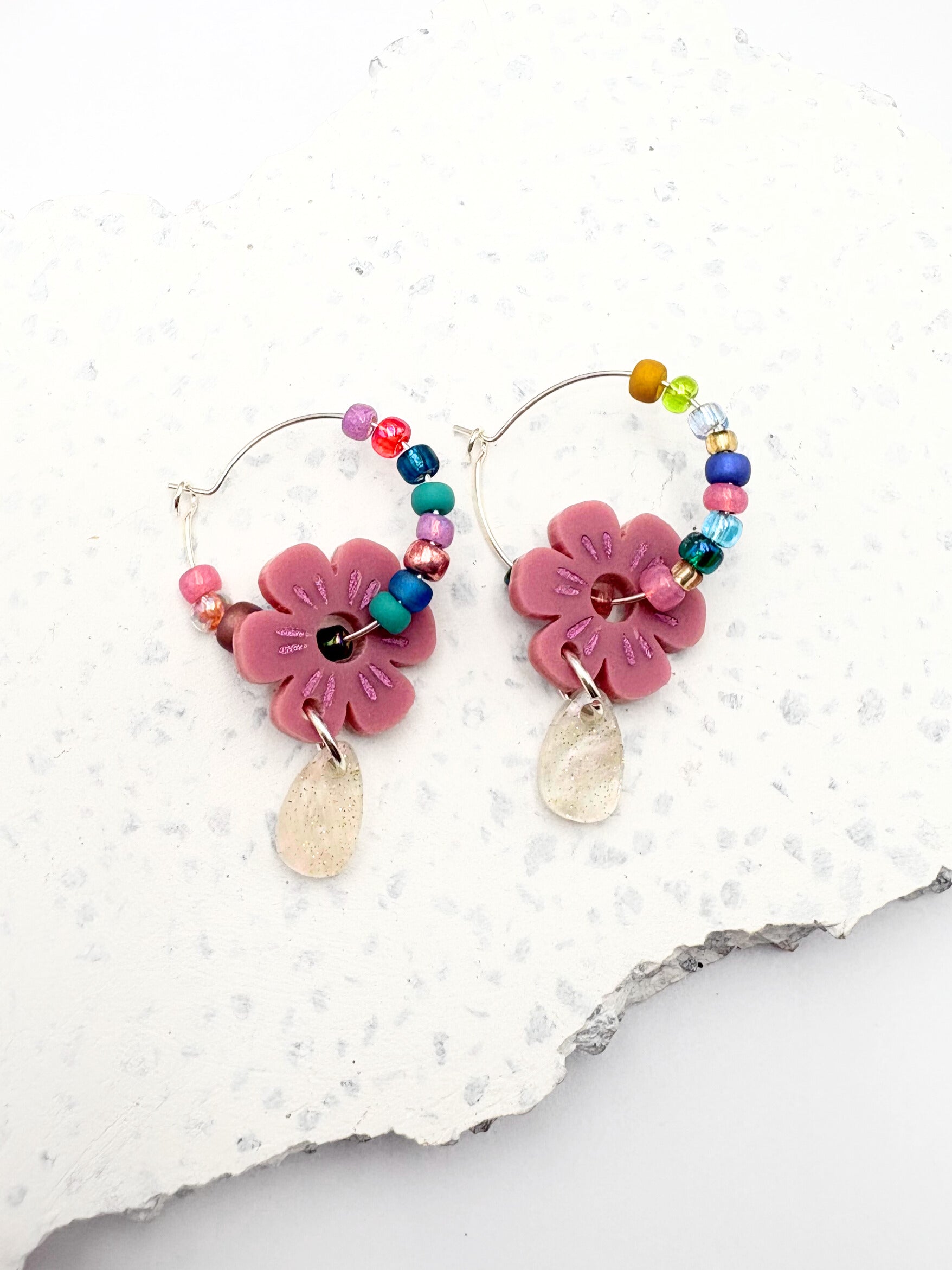 Colorful hoop earrings with pink floral charms on a textured white background
