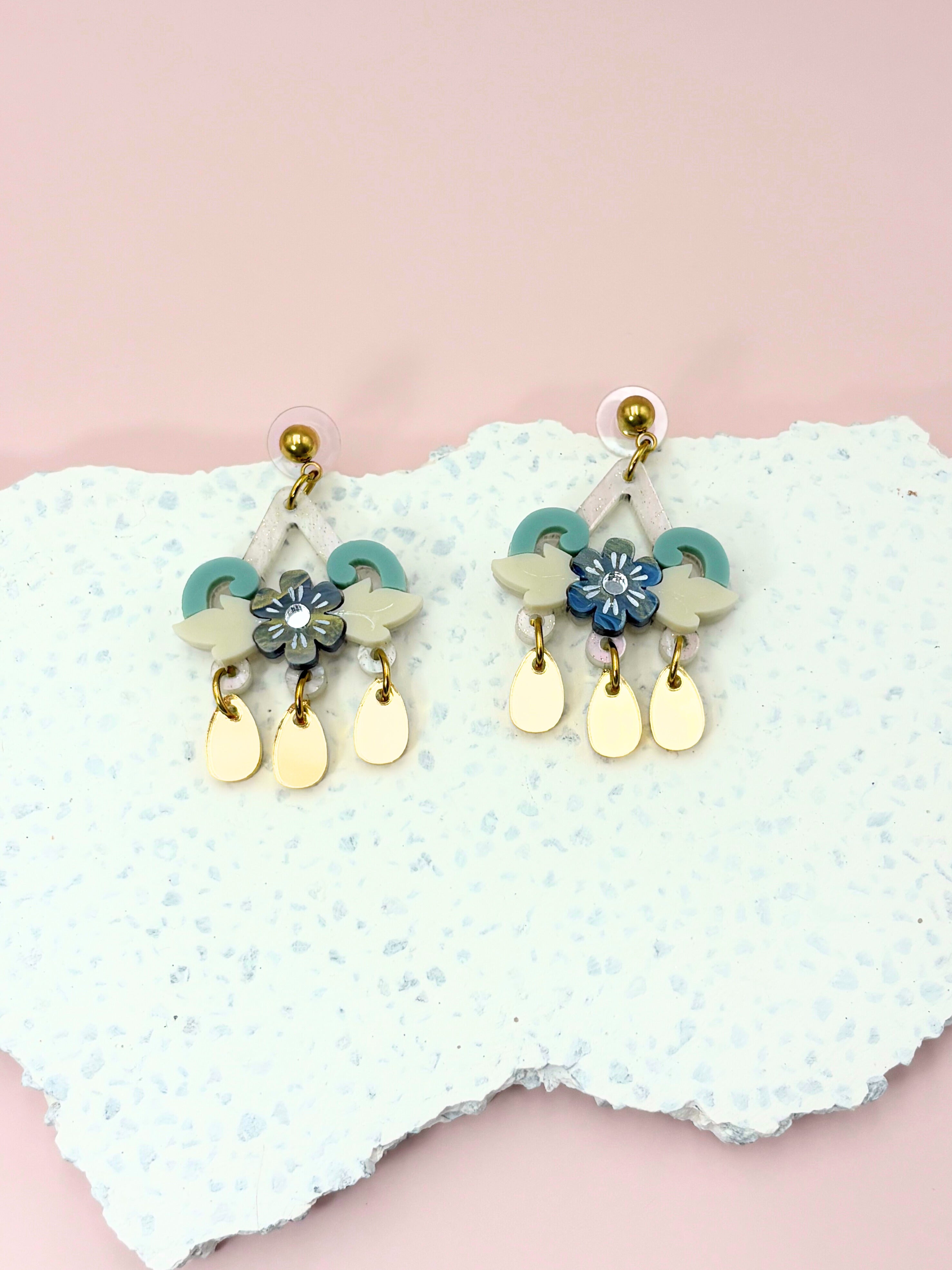 Pair of earrings with floral designs on a textured white surface with a pink background
