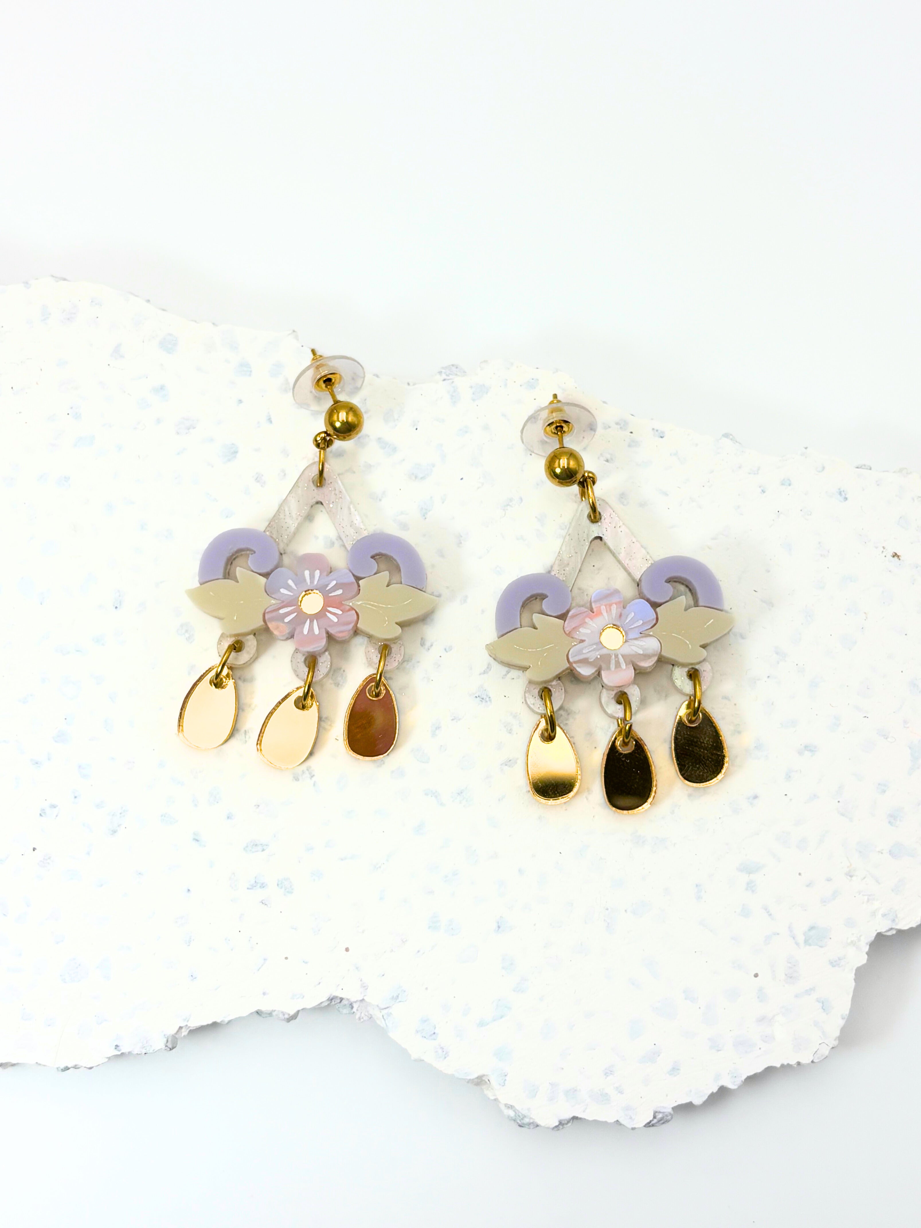 Pair of floral earrings with gold and purple accents on a white stone background