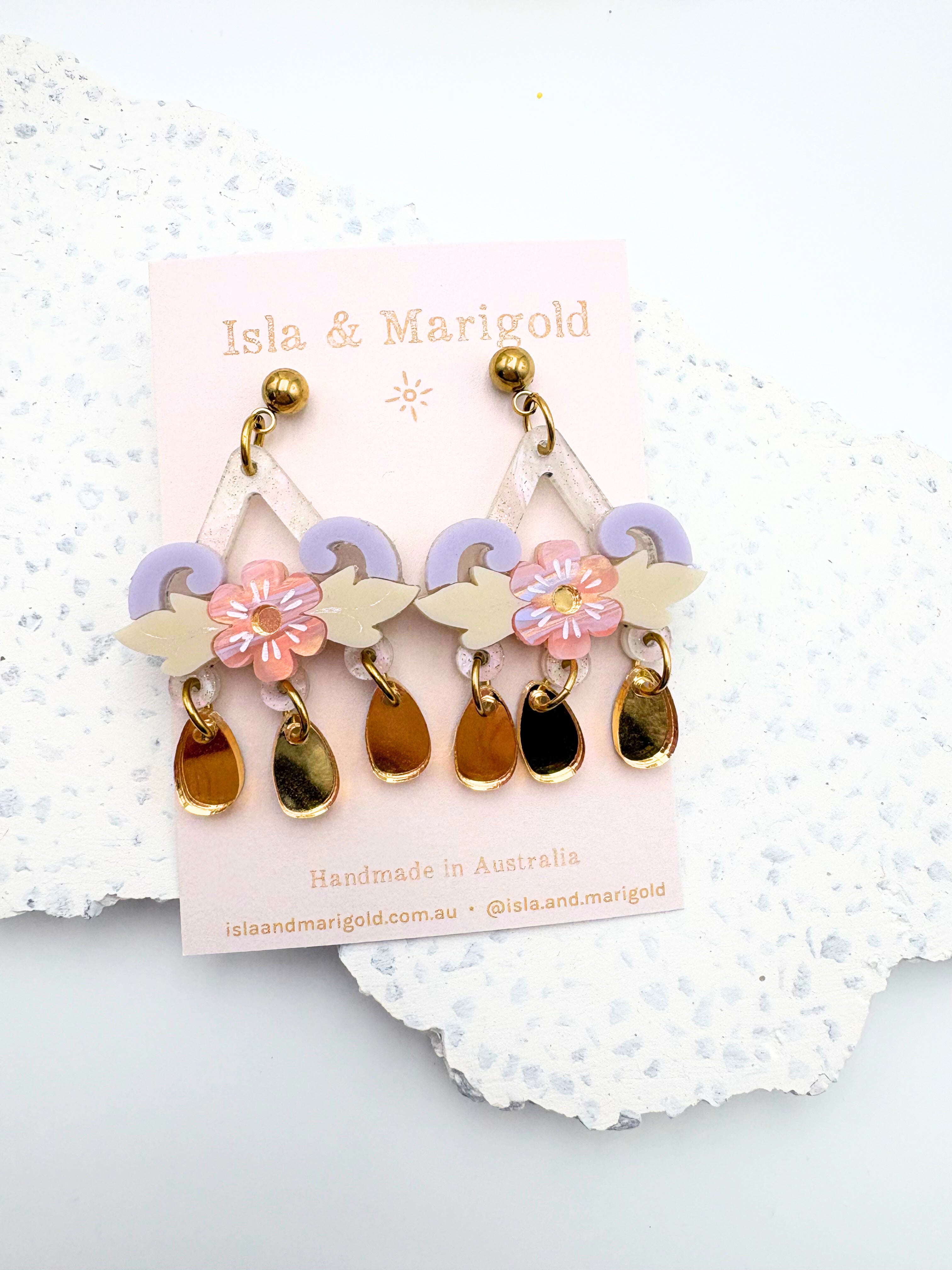 Pair of earrings with floral and leaf designs on a branded card, set against a textured white background.