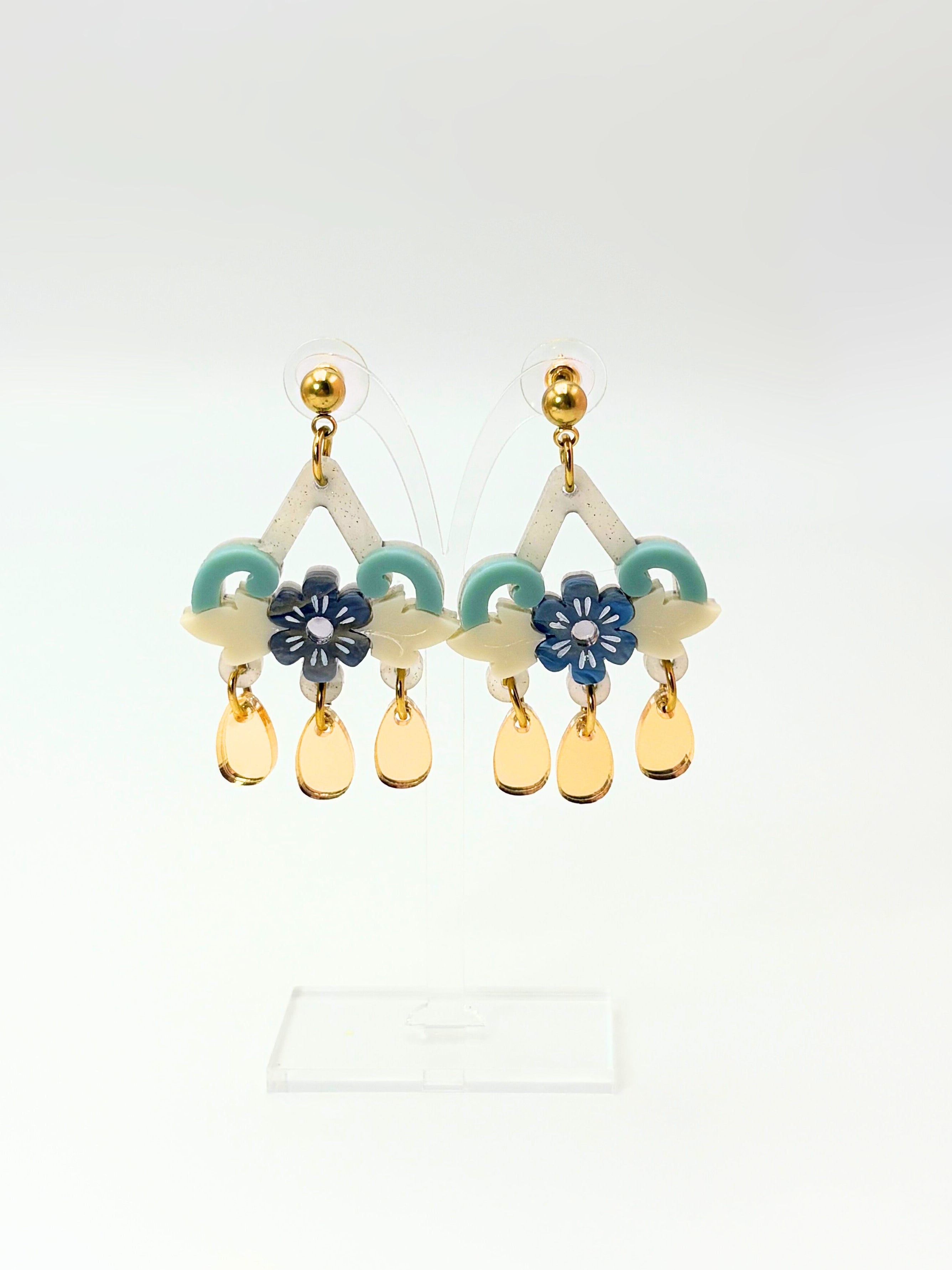 Pair of acrylic and gold earrings with floral and teardrop designs on a white background