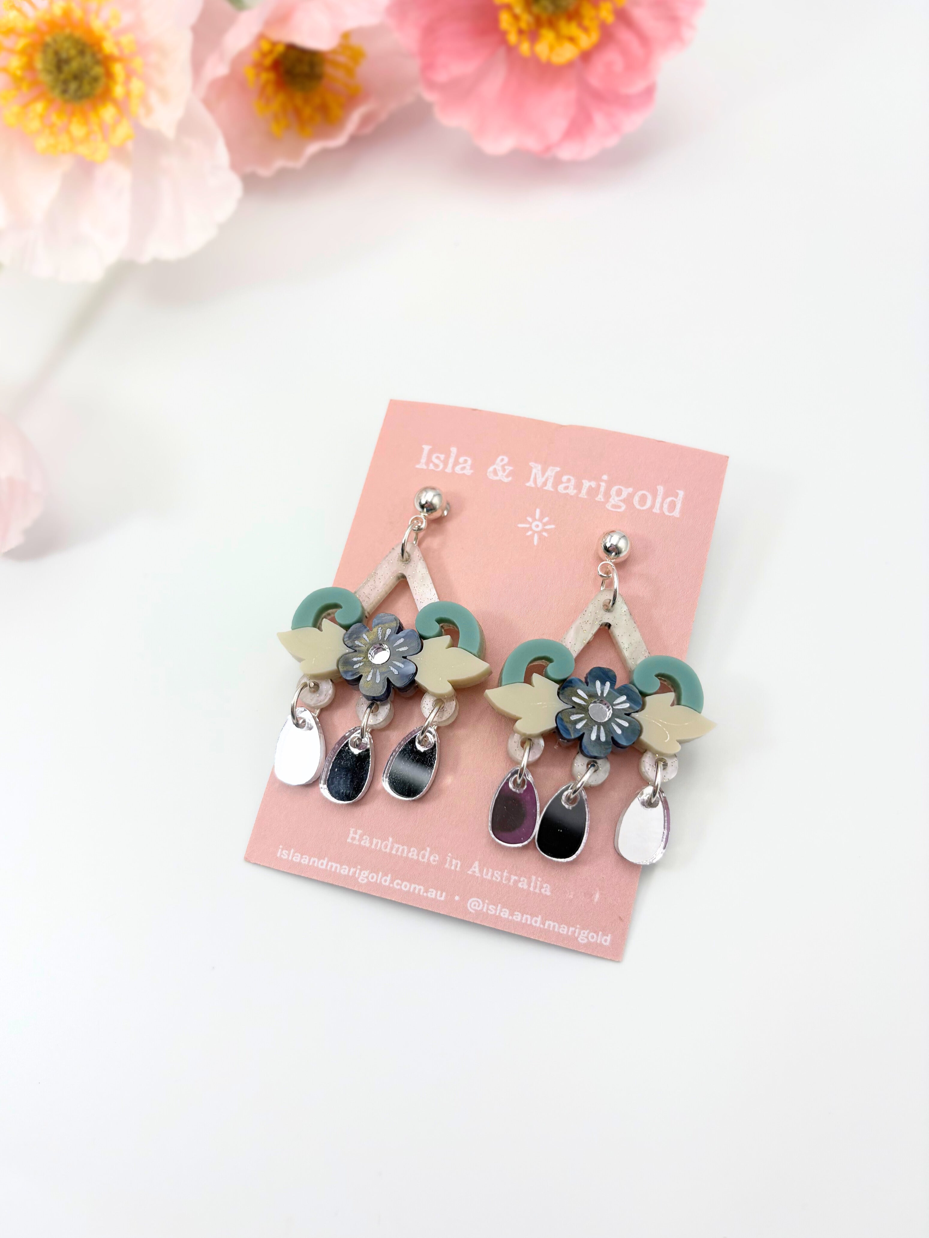 Pair of floral earrings on a pink card with flowers in the background