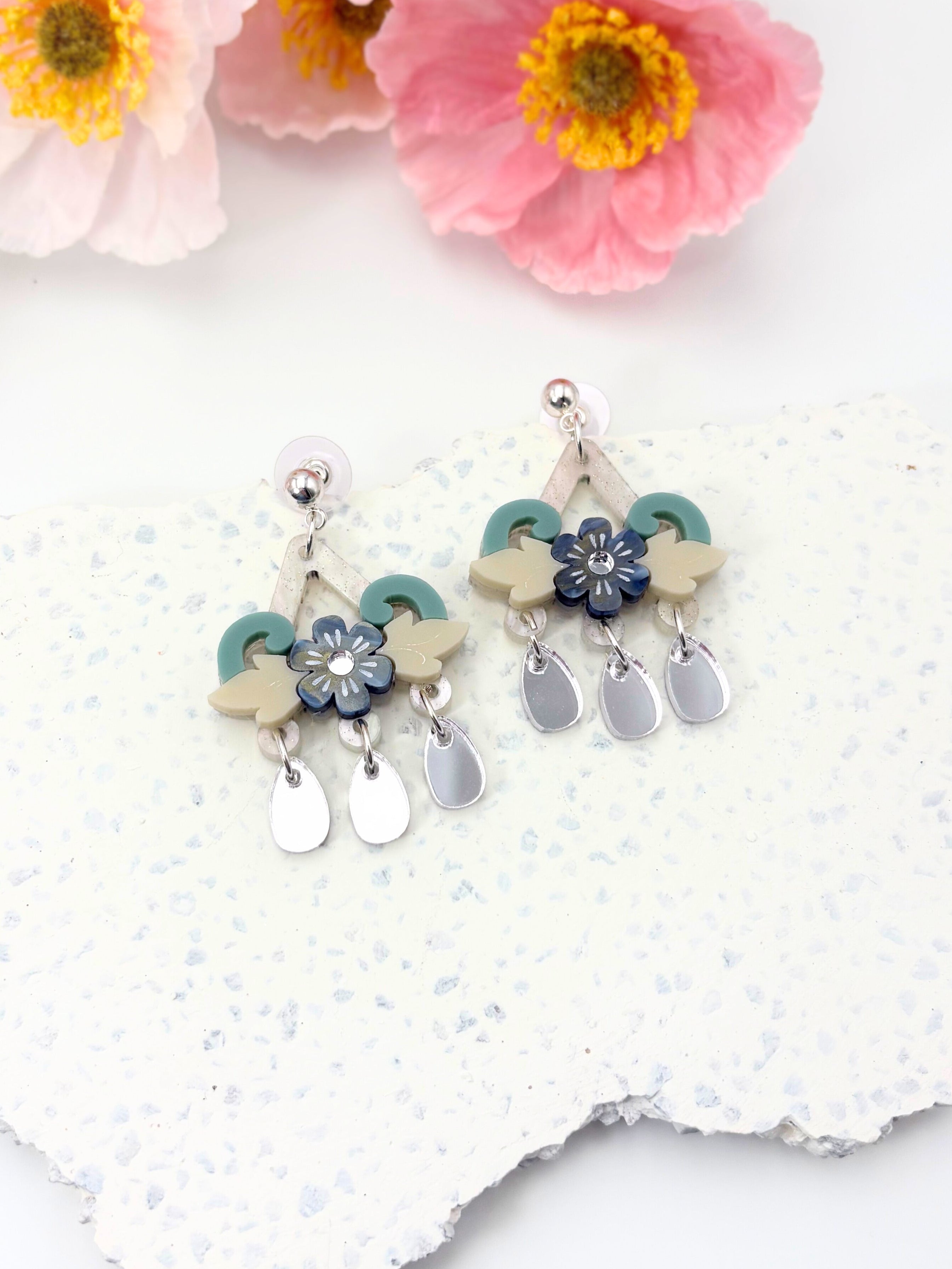Pair of floral earrings on a textured white surface with pink flowers in the background