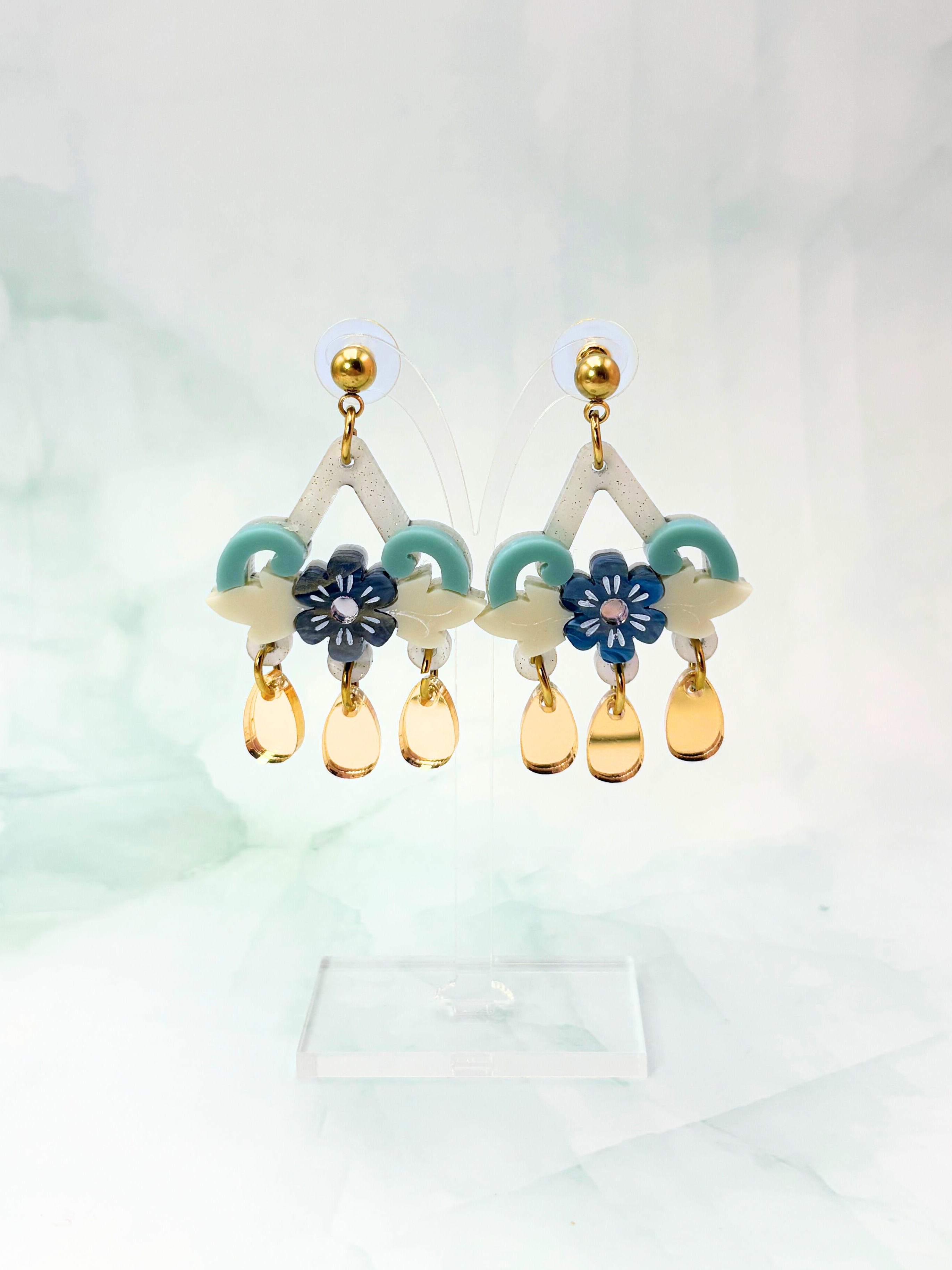 Acrylic  and stainless steel earrings with floral and teardrop designs on a light background