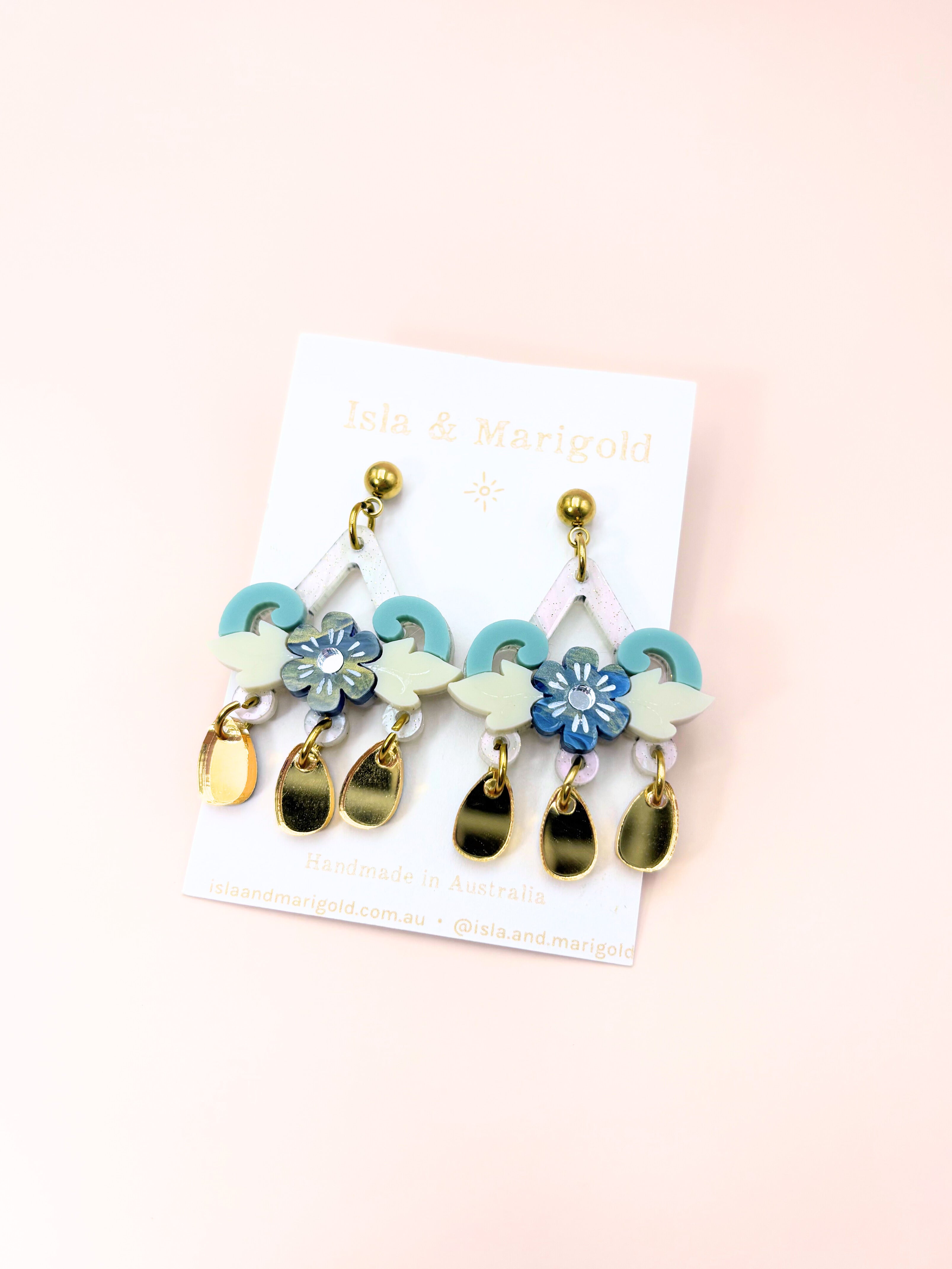 Set of colorful earrings on a branded card against a light pink background